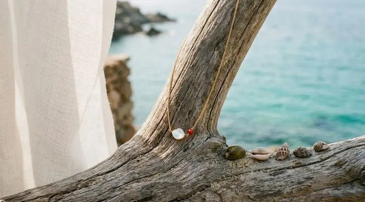 Bijou corse associant nacre blanche et corail rouge, posé sur du bois flotté devant une mer turquoise et un drapé blanc. 